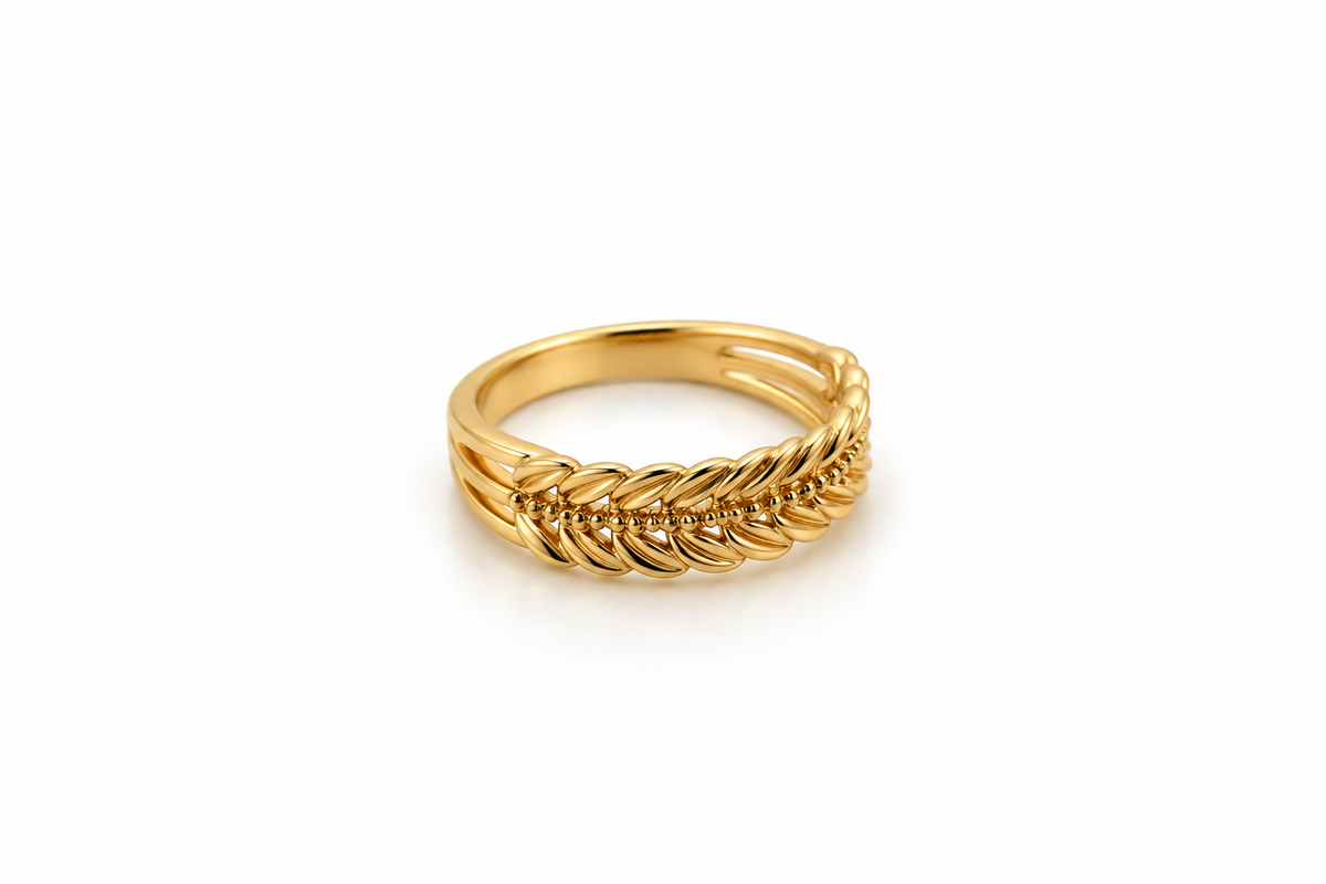 Gold-tone decorative ring with overlapping diagonal leaf-like curves and a central row of small clear stones, shown on a white background and worn on a finger.