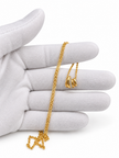 Gold-tone necklace with a fine linked chain and a small layered curved pendant featuring clear reflective stones, displayed on a black jewellery bust and a white gloved hand.