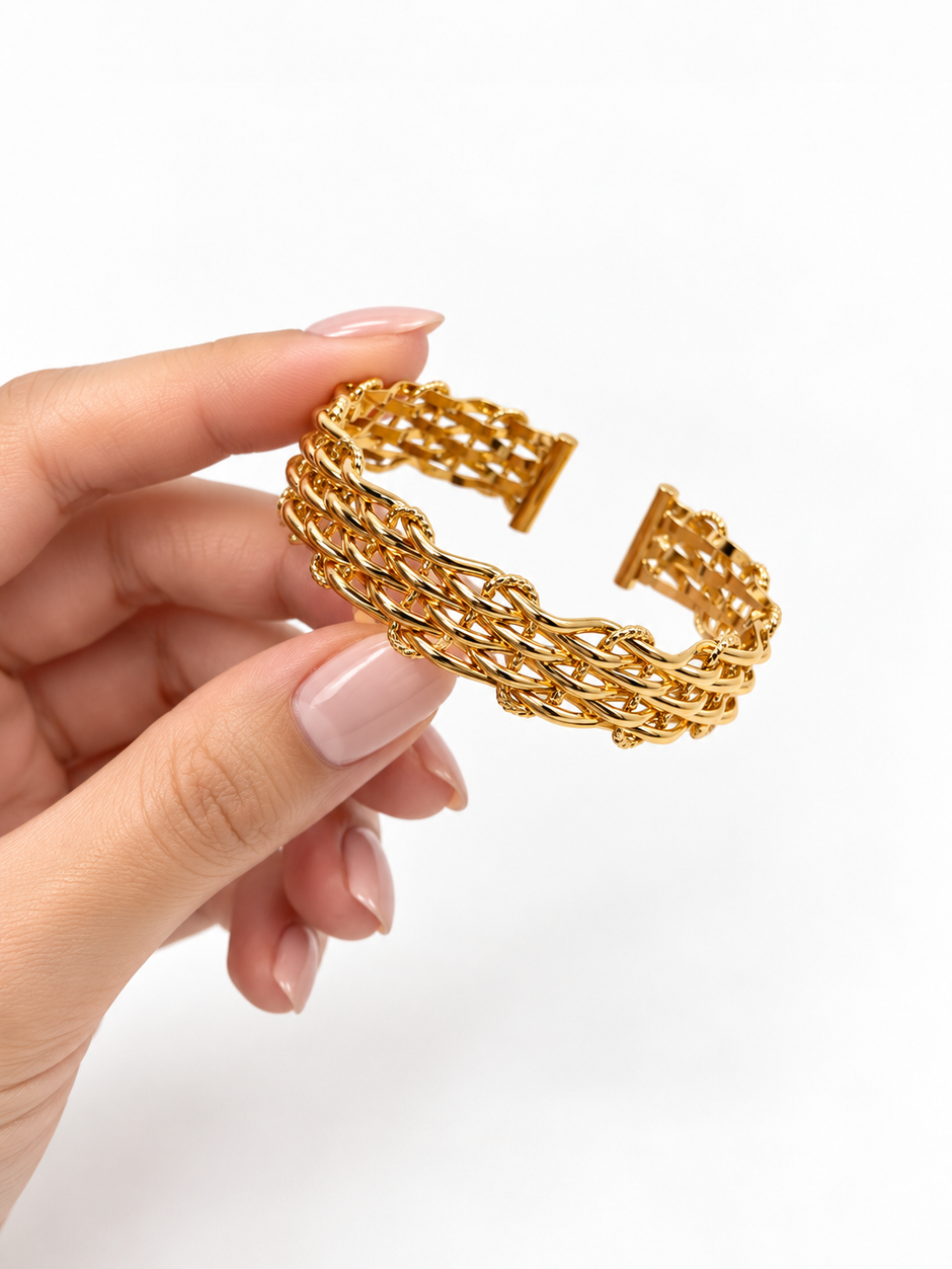 Golden open cuff bracelet featuring an intricate criss-cross lattice band and a rectangular central panel decorated with clear sparkling stones, displayed from the front and back.