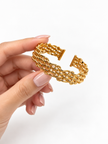 Golden open cuff bracelet featuring an intricate criss-cross lattice band and a rectangular central panel decorated with clear sparkling stones, displayed from the front and back.