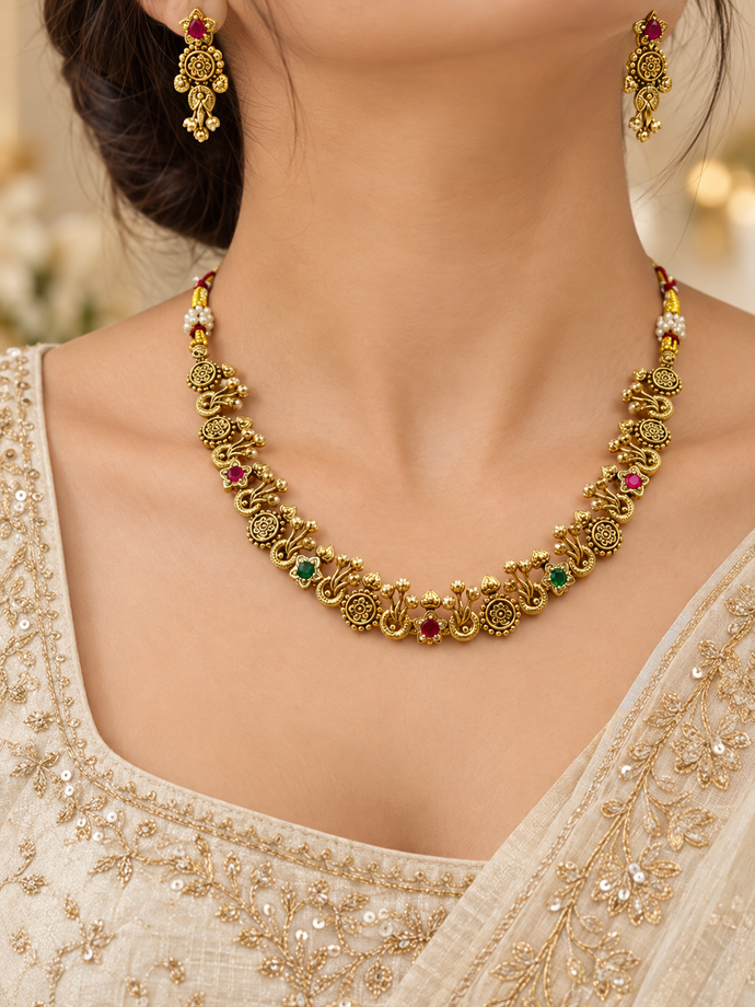 Traditional gold-tone floral necklace set with matching dangling earrings, featuring magenta and green accents, ivory-white bead-like details and intricate ornamental motifs.