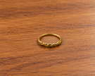 Gold-tone ring with a slender band, flowing interlacing wave pattern and small clear reflective accents, displayed on a white background and worn on a finger.