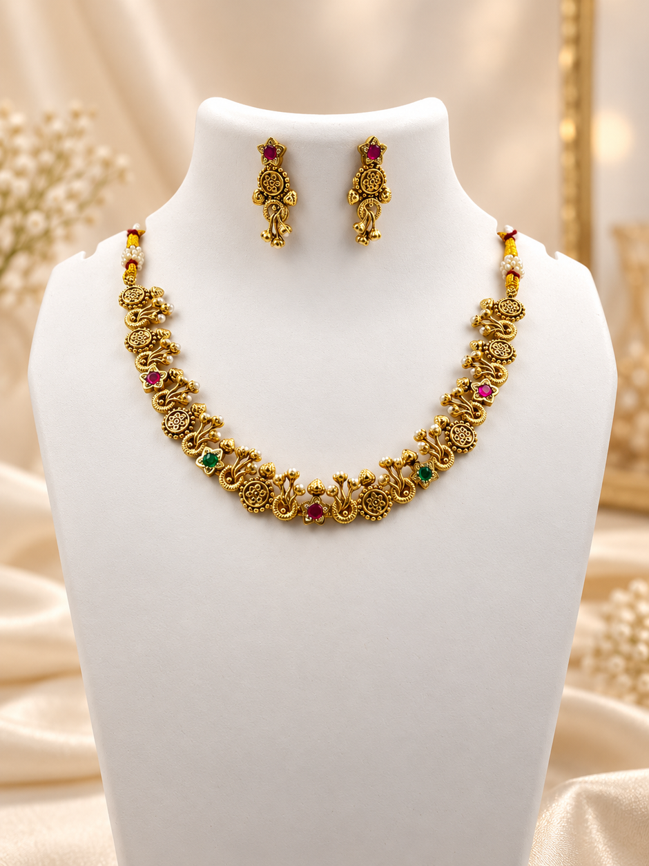 Traditional gold-tone floral necklace set with matching dangling earrings, featuring magenta and green accents, ivory-white bead-like details and intricate ornamental motifs.
