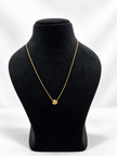 Gold-tone necklace with a fine linked chain and a small layered curved pendant featuring clear reflective stones, displayed on a black jewellery bust and a white gloved hand.