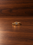 Gold-tone ring with a round floral arrangement of clear stones, curved golden detailing and small clear accents along the band, shown on a white background and worn on a finger.