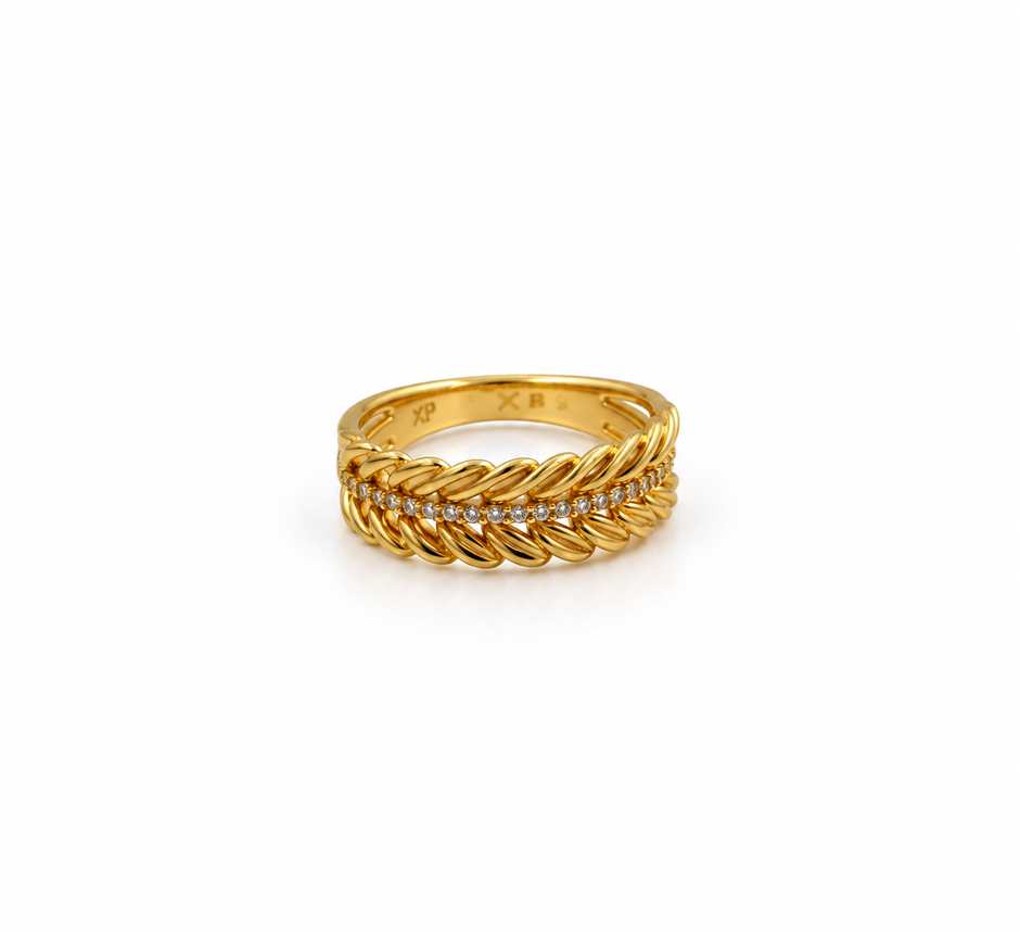 Gold-tone decorative ring with overlapping diagonal leaf-like curves and a central row of small clear stones, shown on a white background and worn on a finger.
