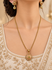 Gold-tone floral halo necklace set displayed on white jewellery stands, featuring a round pendant with green and magenta-pink accents, a decorative beaded chain, and matching earrings with green teardrop-shaped drops.