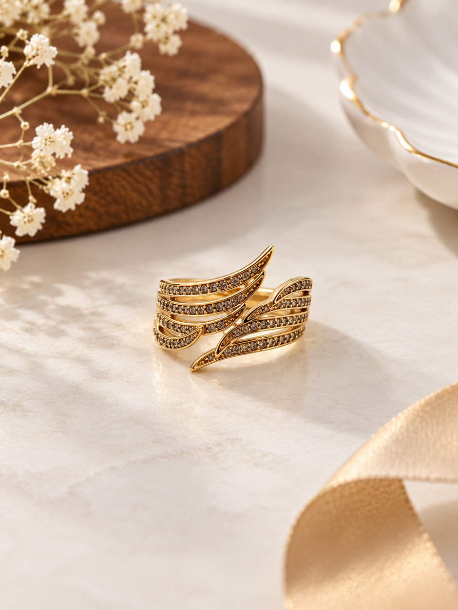 Gold-tone multi-row crossover ring with intertwined curved bands, round clear stones and dark accent detailing on a white background.