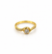 Gold-tone ring with a round floral arrangement of clear stones, curved golden detailing and small clear accents along the band, shown on a white background and worn on a finger.