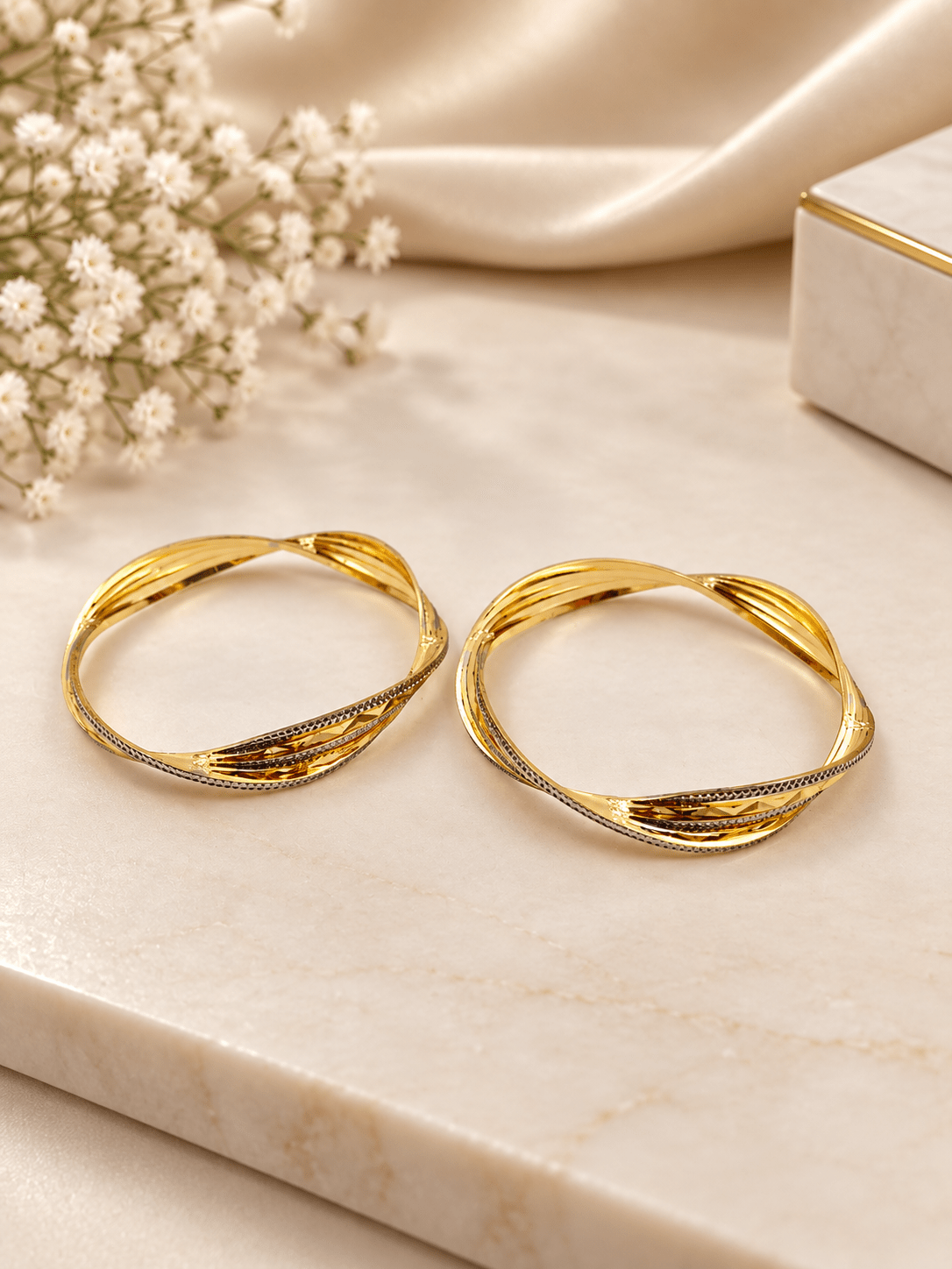 Pair of golden-toned twisted bangles with layered curved bands and contrasting textured detailing