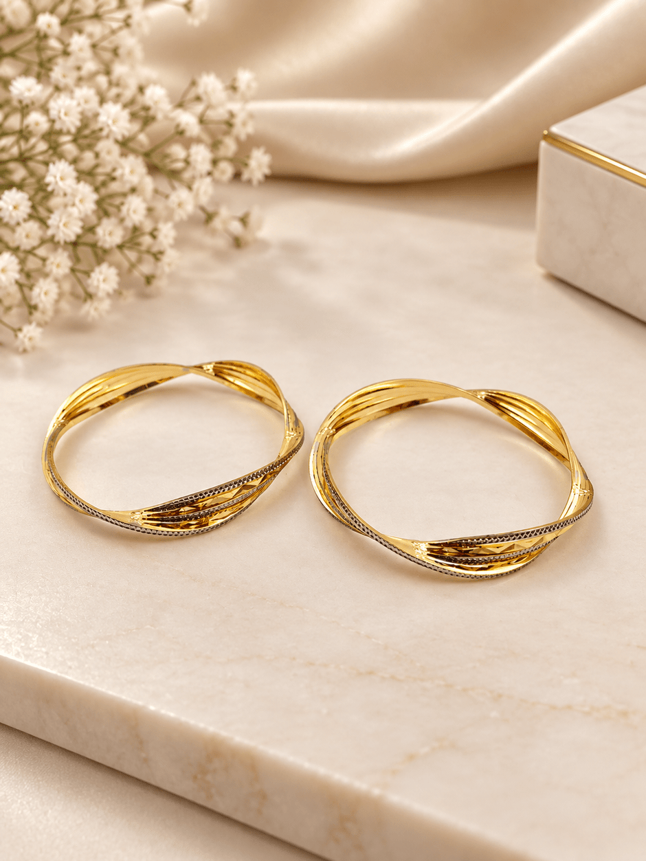 Pair of golden-toned twisted bangles with layered curved bands and contrasting textured detailing