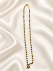 Black beaded necklace with small gold-tone connecting elements and a gold-tone clasp, displayed as an elongated chain on a white background and held in a white-gloved hand. - bhavmayi
