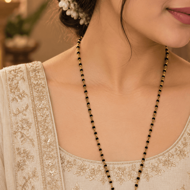 Woman wearing a long black-beaded necklace with delicate gold-tone links, styled with a cream embroidered traditional outfit.
