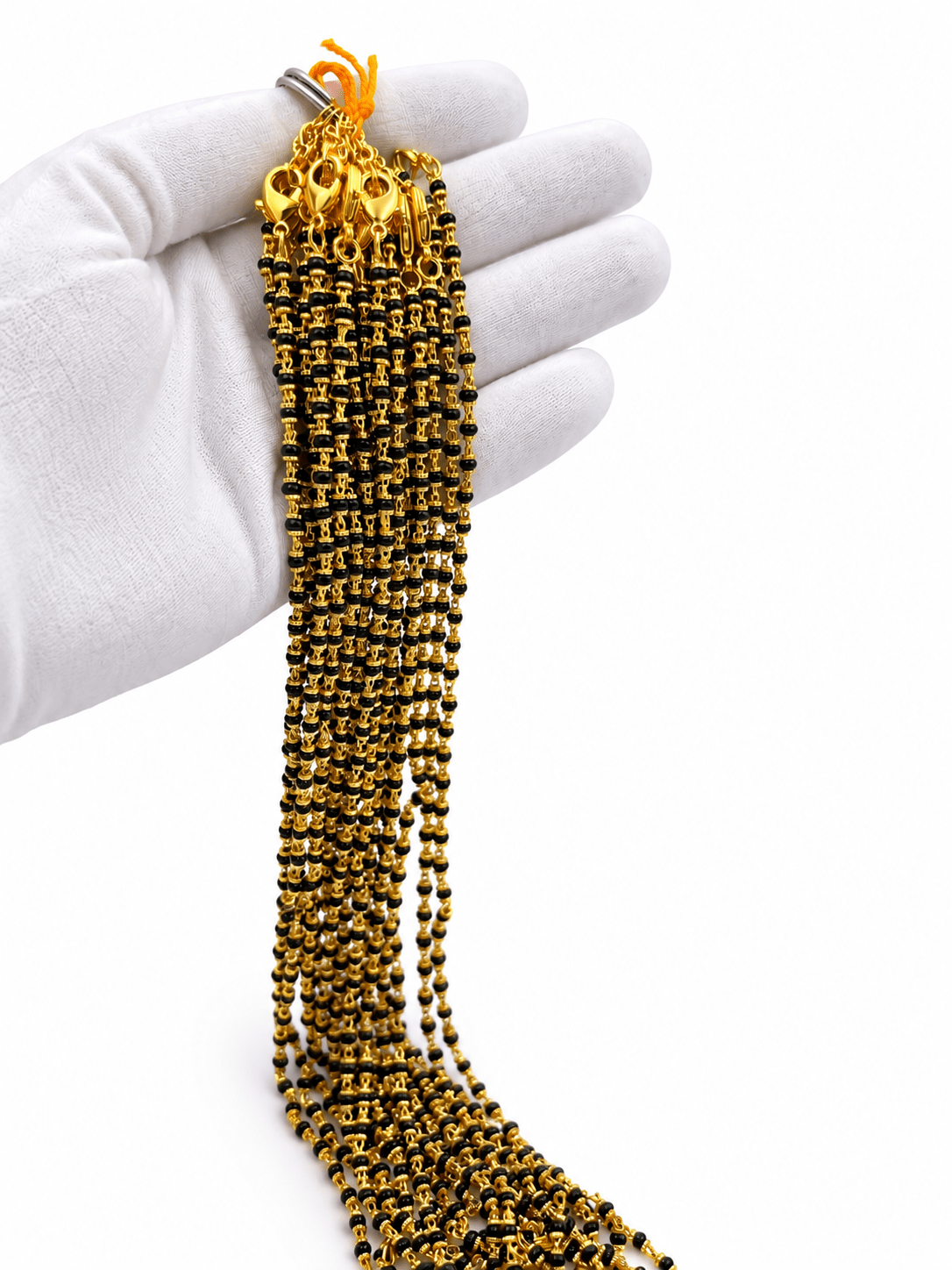 Black beaded necklace with small gold-tone connecting elements and a gold-tone clasp, displayed as an elongated chain on a white background and held in a white-gloved hand. - bhavmayi