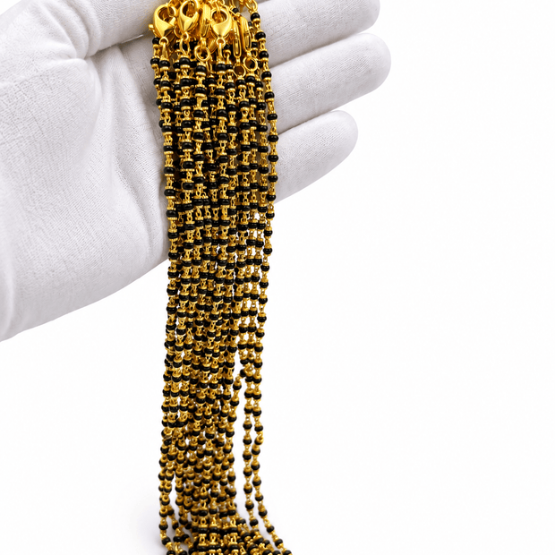 Woman wearing a long black-beaded necklace with delicate gold-tone links, styled with a cream embroidered traditional outfit.