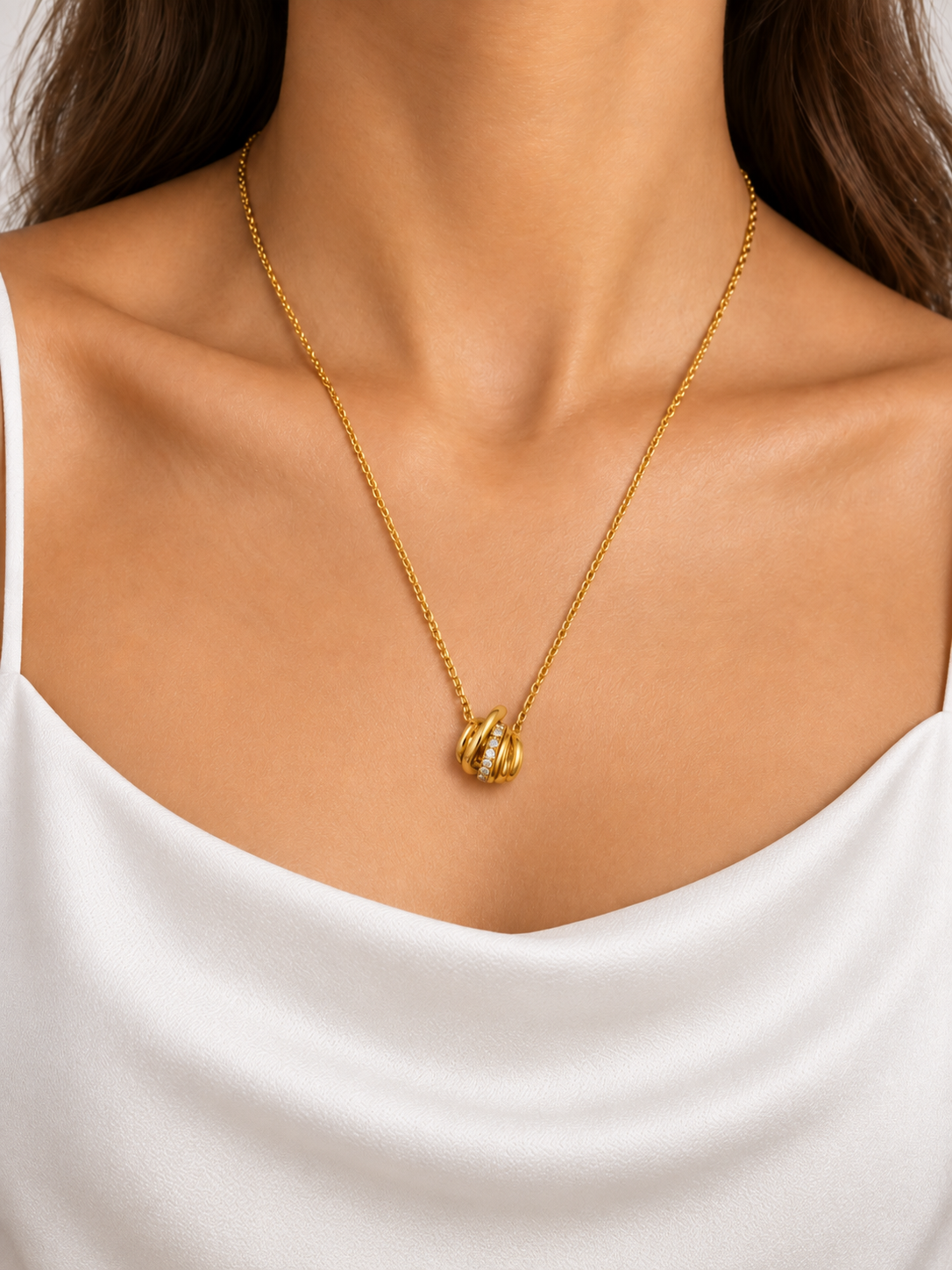 Gold-tone necklace with a fine linked chain and a small layered curved pendant featuring clear reflective stones, displayed on a black jewellery bust and a white gloved hand.