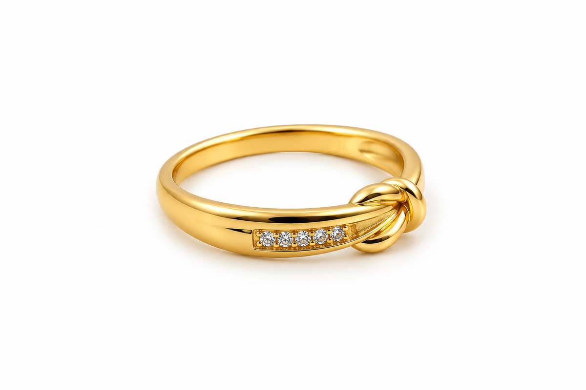 Gold-tone knot ring featuring intertwined curved loops, a row of small clear stones and dark accents, shown on a finger and from the side.