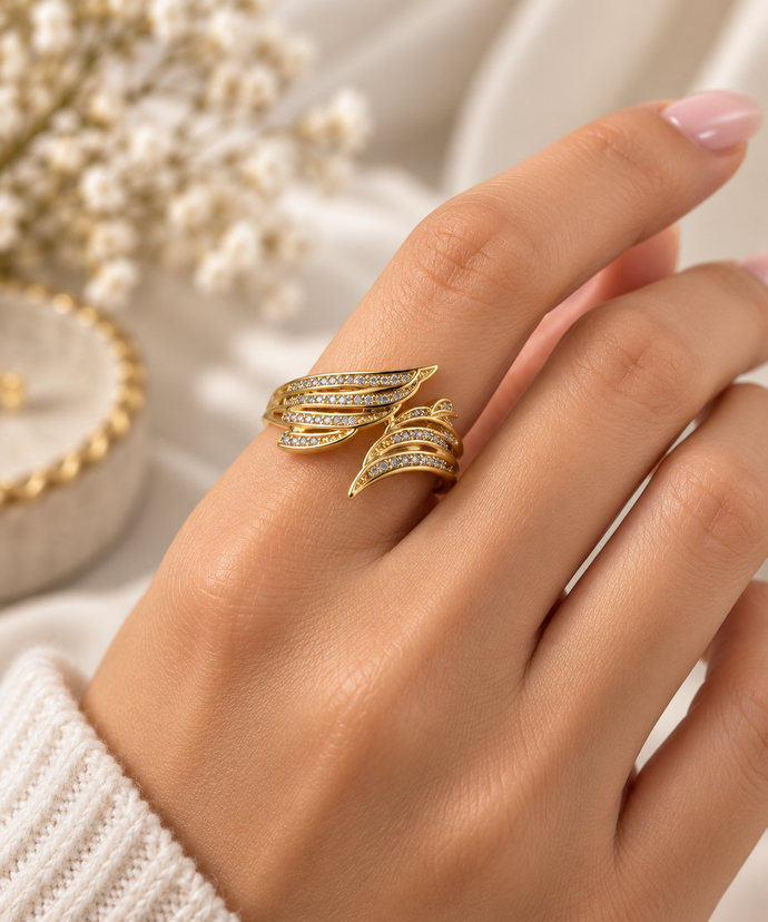 Gold-tone multi-row crossover ring with intertwined curved bands, round clear stones and dark accent detailing on a white background.