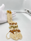 Double-strand white beaded necklace with deep red and green bead accents, decorative gold-tone elements and a gold-tone clasp displayed on a white necklace stand. - bhavmayi