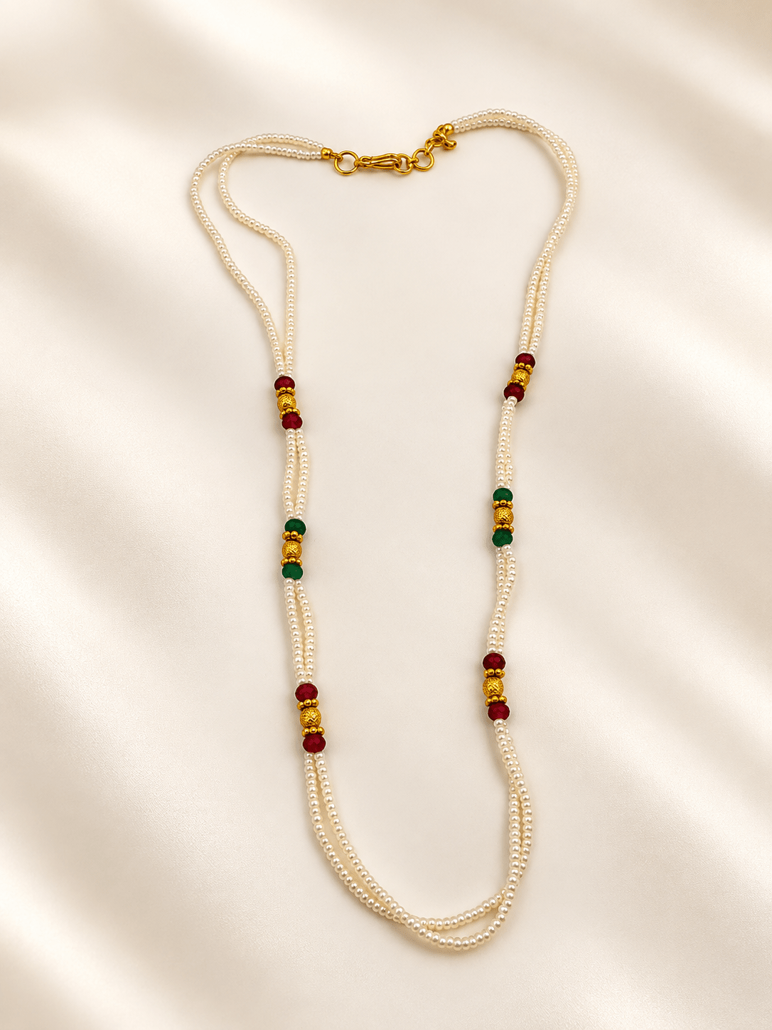 Double-strand white beaded necklace with deep red and green bead accents, decorative gold-tone elements and a gold-tone clasp displayed on a white necklace stand. - bhavmayi
