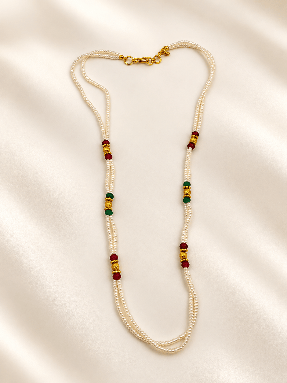 Double-strand white beaded necklace with deep red and green bead accents, decorative gold-tone elements and a gold-tone clasp displayed on a white necklace stand. - bhavmayi