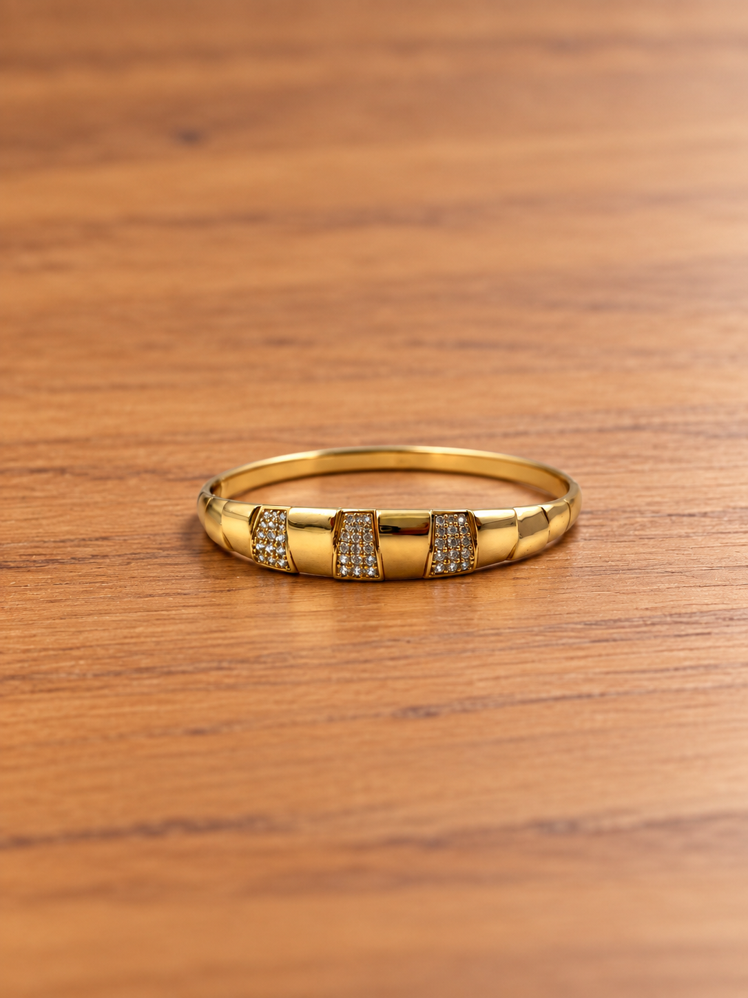 Gold-tone wide band bracelet displayed against a white background, featuring three rectangular front panels decorated with rows of clear accents and smooth golden sections.
