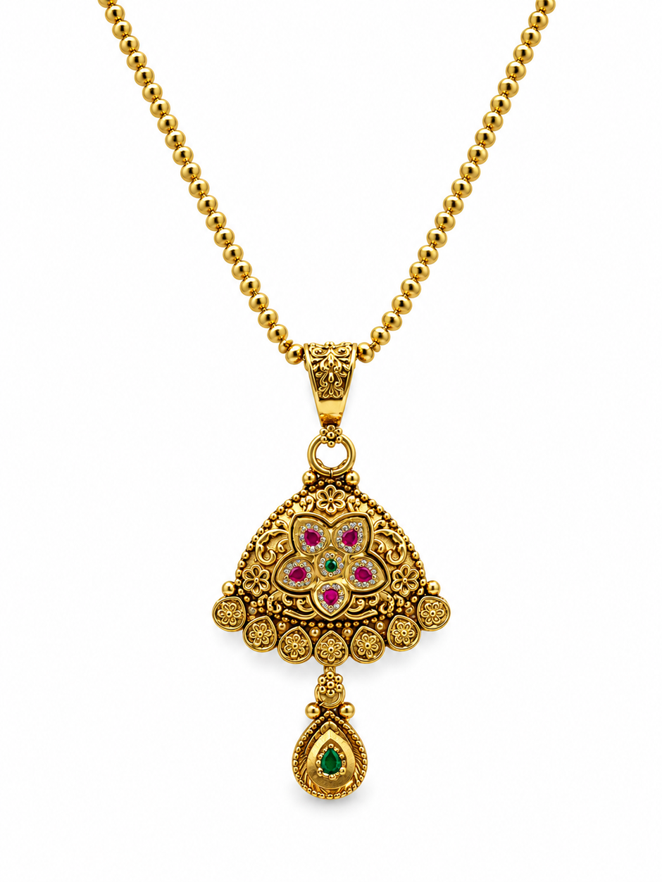 Gold-tone floral temple necklace set displayed on white jewellery stands, featuring a triangular ornamental pendant with green and magenta-pink accents, a beaded chain, and matching earrings with green teardrop-shaped drops.