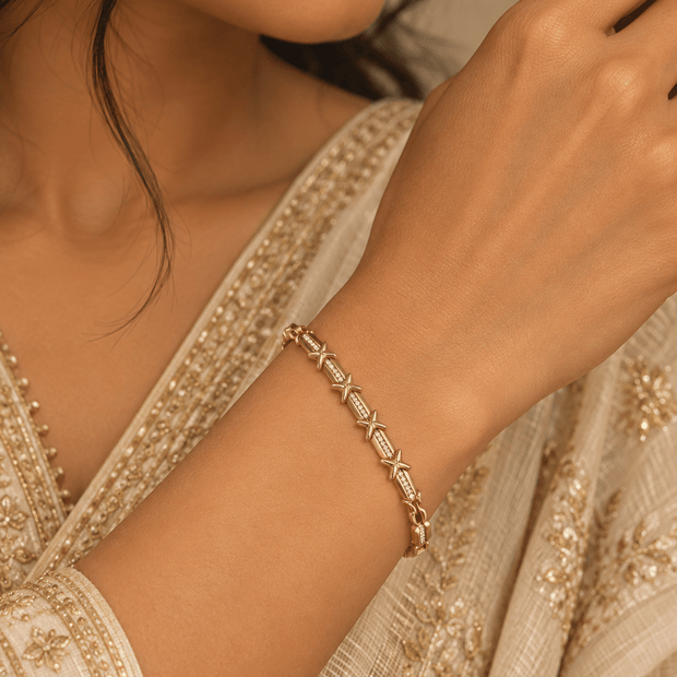 Golden bracelet featuring repeated X-shaped motifs, clear accent detailing and structured clasp links