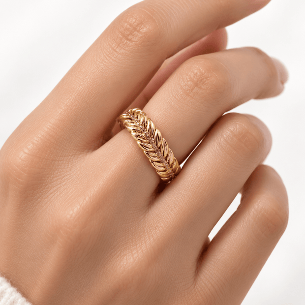 Gold-tone decorative ring with overlapping diagonal leaf-like curves and a central row of small clear stones, shown on a white background and worn on a finger. - bhavmayi