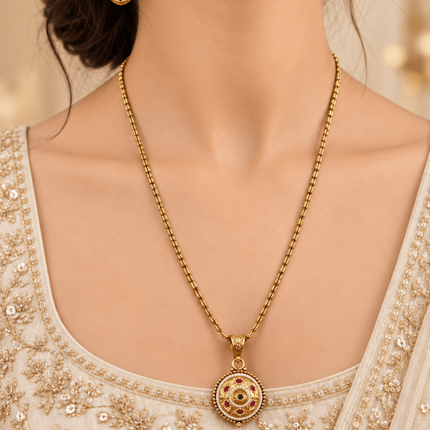 Gold-tone floral halo necklace set displayed on white jewellery stands, featuring a round pendant with green and magenta-pink accents, a decorative beaded chain, and matching earrings with green teardrop-shaped drops. - bhavmayi