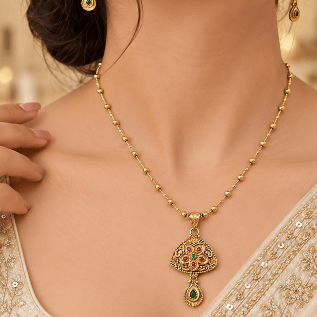 Gold-tone floral temple necklace set with green and magenta accents, featuring a pendant and matching drop earrings.