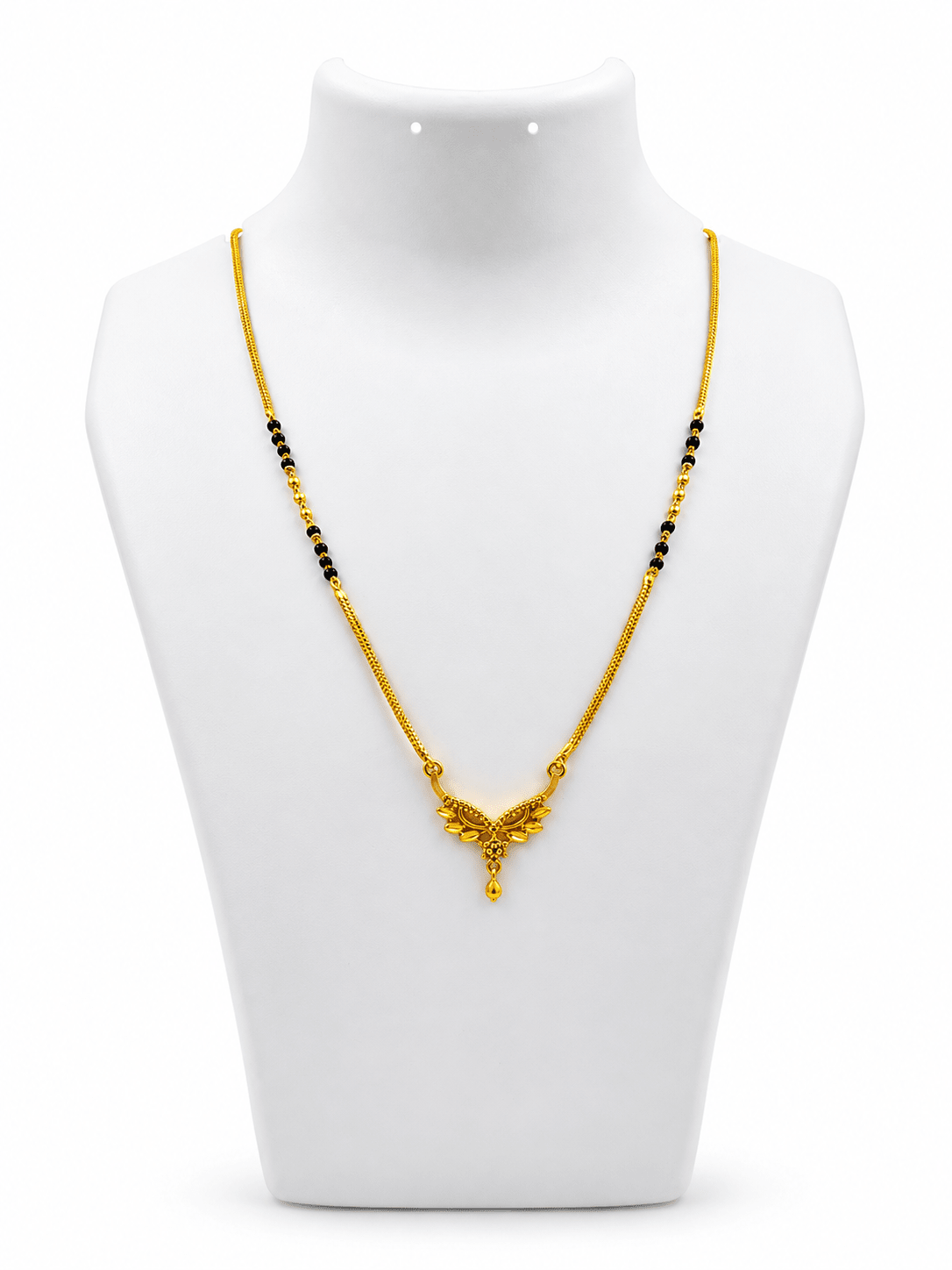 Gold-tone mangalsutra necklace with black beads, symmetrical floral leaf-shaped centerpiece, clear decorative stones, red center accent, and dangling teardrop pendant on a white background. - bhavmayi