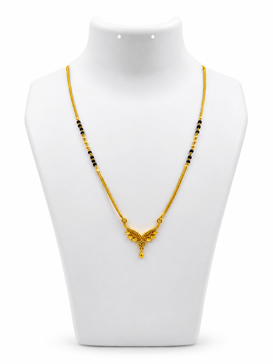 Gold-tone mangalsutra necklace with black beads, symmetrical floral leaf-shaped centerpiece, clear decorative stones, red center accent, and dangling teardrop pendant on a white background. - bhavmayi