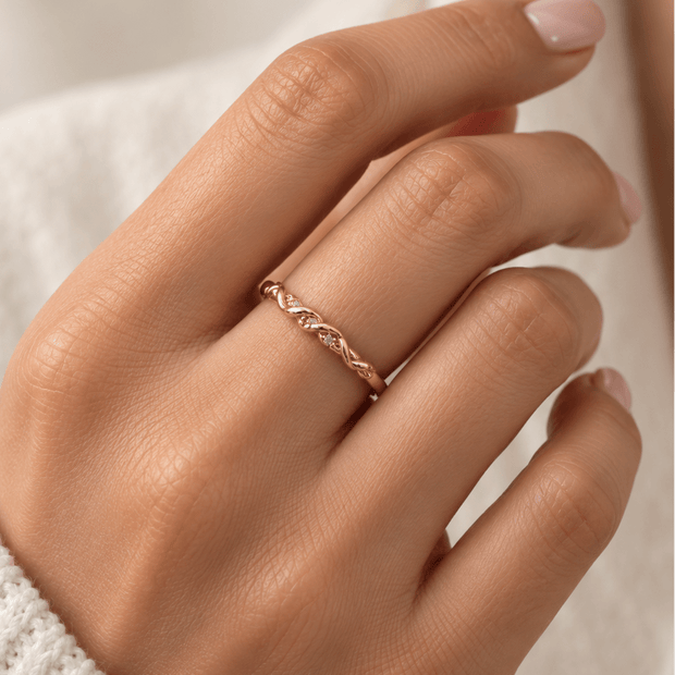 Gold-tone ring with a slender band, flowing interlacing wave pattern and small clear reflective accents, displayed on a white background and worn on a finger. - bhavmayi