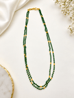 Green beaded necklace with small gold-tone connecting elements and a gold-tone clasp, displayed in a rounded elongated shape on a white jewellery display and against an elegant neutral background. - bhavmayi