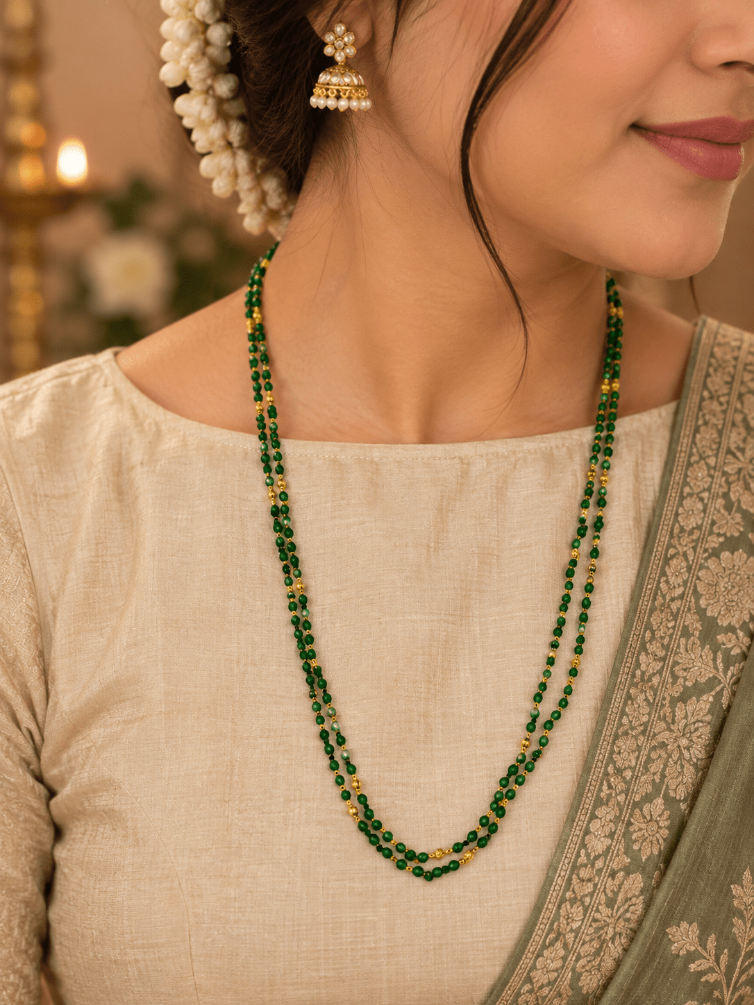 Green beaded necklace with small gold-tone connecting elements and a gold-tone clasp, displayed in a rounded elongated shape on a white jewellery display and against an elegant neutral background. - bhavmayi