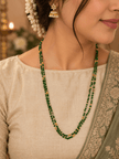 Green beaded necklace with small gold-tone connecting elements and a gold-tone clasp, displayed in a rounded elongated shape on a white jewellery display and against an elegant neutral background. - bhavmayi