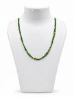 Green beaded necklace with small gold-tone connecting elements and a gold-tone clasp, displayed in a rounded elongated shape on a white jewellery display and against an elegant neutral background. - bhavmayi