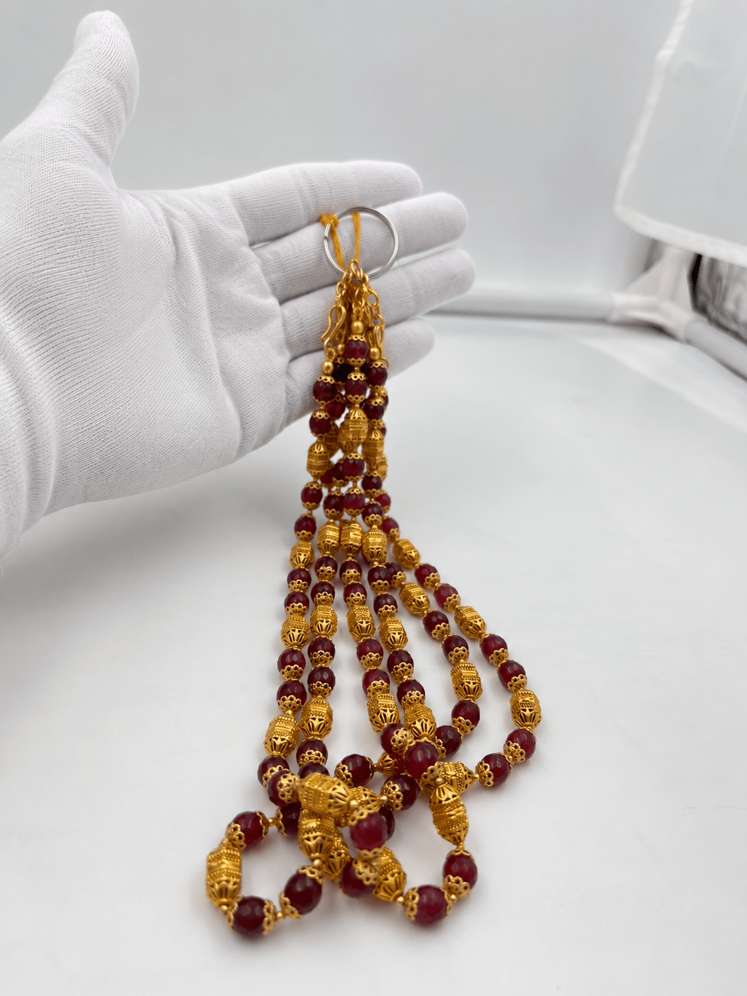Long maroon beaded necklace with glossy rounded beads, ornate gold-tone barrel-shaped beads, floral-style bead caps and a hook-style clasp, shown from two angles. - bhavmayi