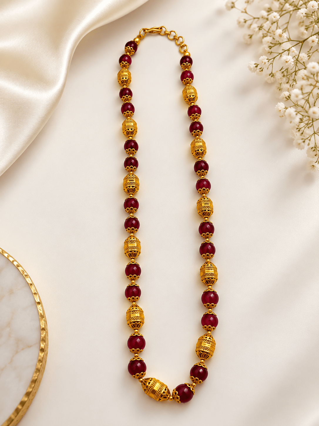 Long maroon beaded necklace with glossy rounded beads, ornate gold-tone barrel-shaped beads, floral-style bead caps and a hook-style clasp, shown from two angles. - bhavmayi