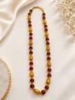 Long maroon beaded necklace with glossy rounded beads, ornate gold-tone barrel-shaped beads, floral-style bead caps and a hook-style clasp, shown from two angles. - bhavmayi