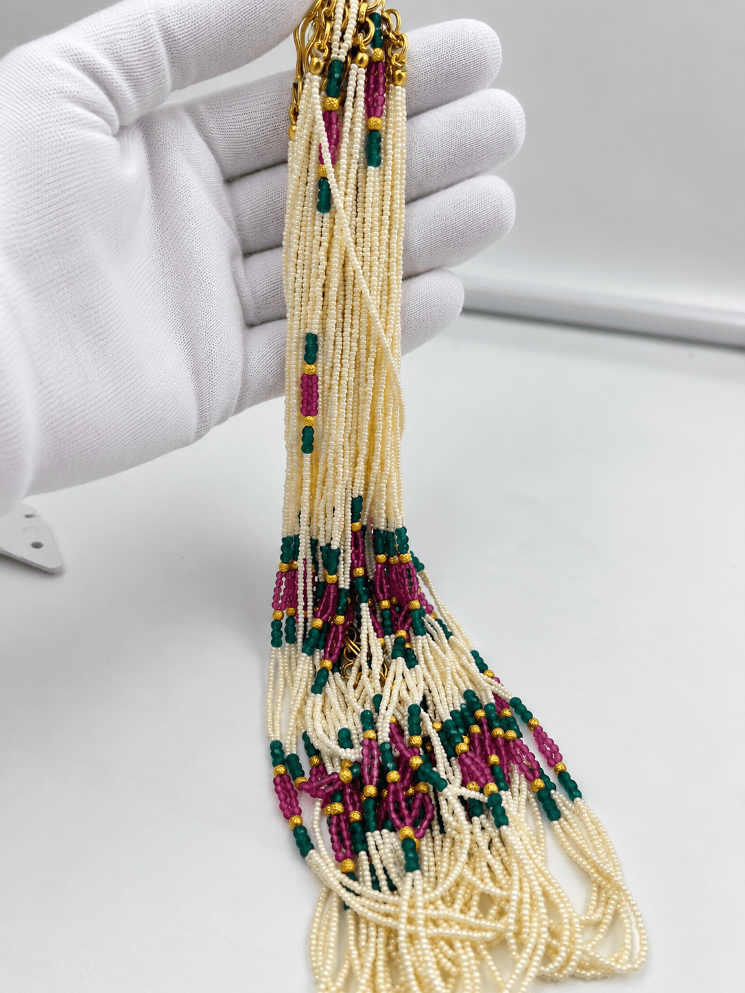 Long multistrand ivory-white pearl-style beaded necklace with green and magenta pink bead sections, gold-tone decorative accents and a hook-style clasp, shown from two angles. - bhavmayi