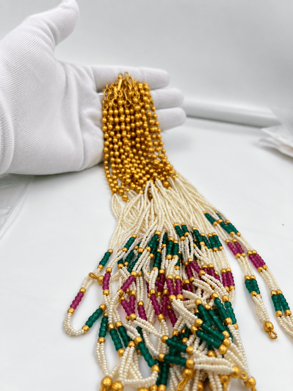 Long multistrand ivory-white pearl-style necklace featuring round gold-tone beads, green and magenta bead sections, and a gold-tone hook clasp, shown from two angles. - bhavmayi