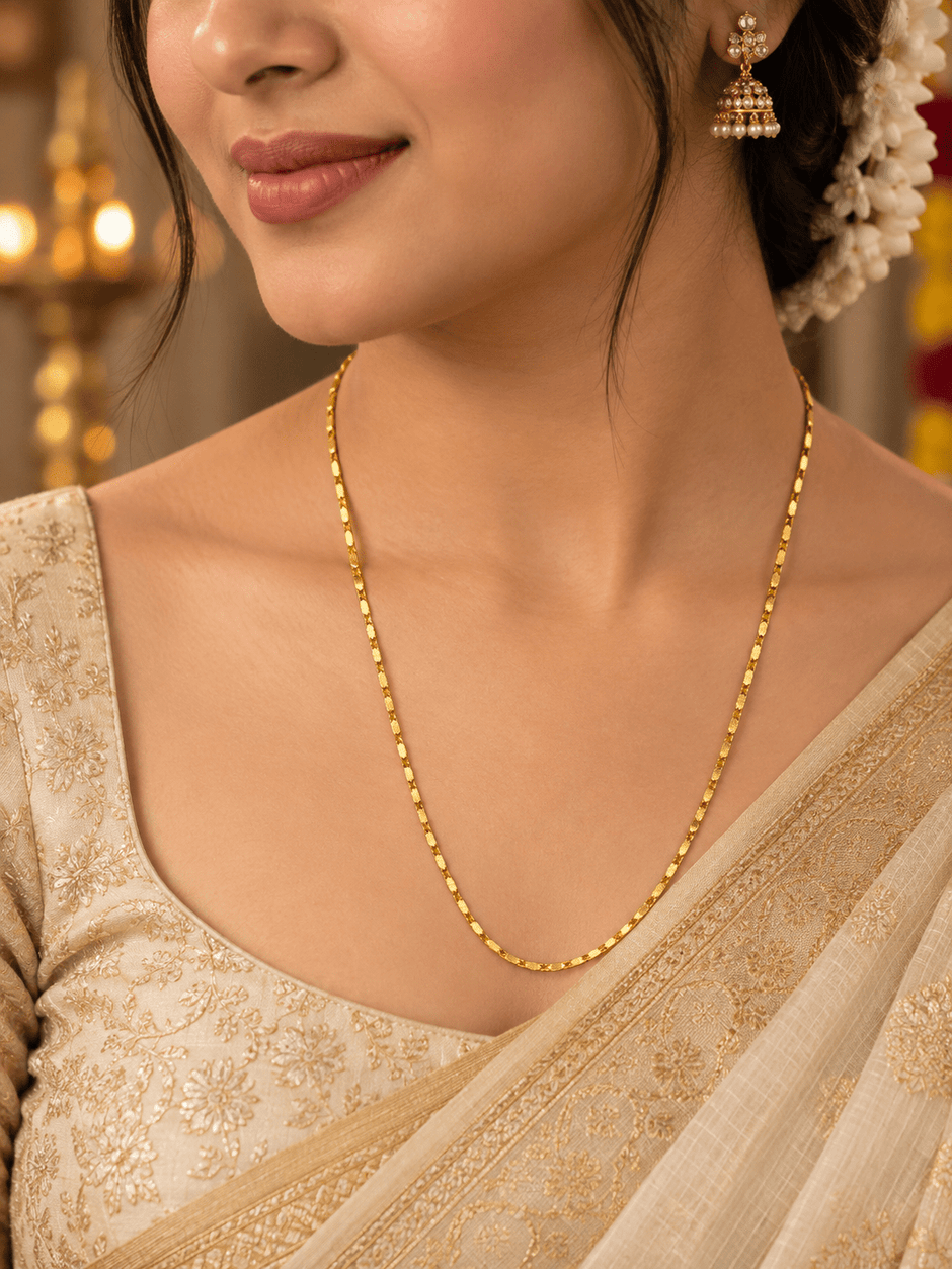Slender golden chain necklace with repeating small geometric links displayed in a U shape and on a white necklace bust. - bhavmayi