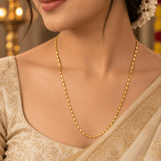 Delicate yellow gold-tone chain necklace with a repeating textured link pattern, on a white necklace stand by Bhavmayi.