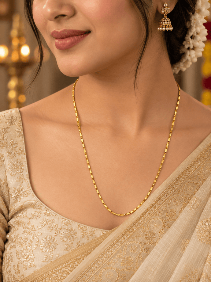 Slender golden chain necklace with repeating small geometric links displayed in a U shape and on a white necklace bust. - bhavmayi